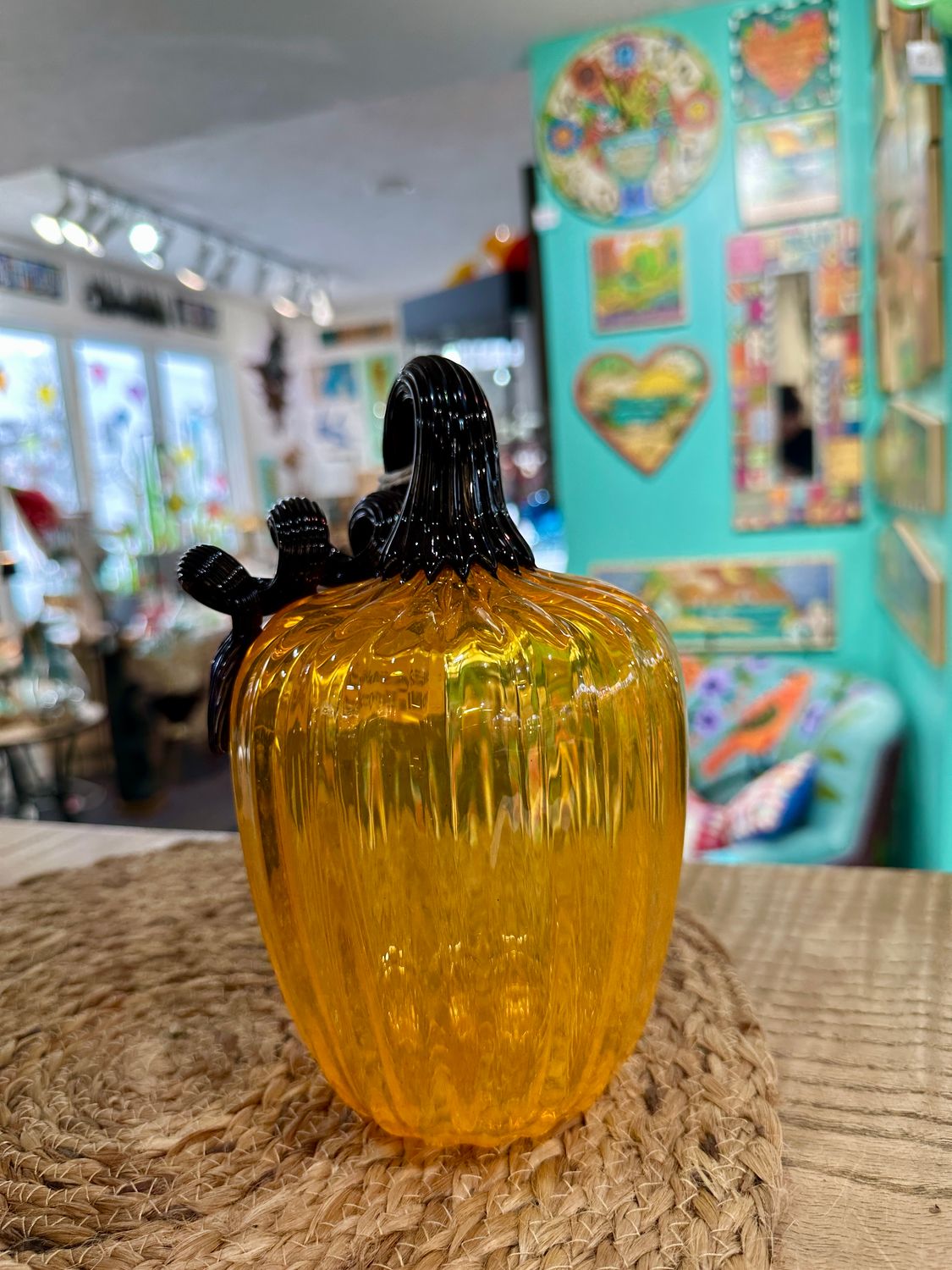 Large hand-blown glass pumpkin sculpture in vibrant golden amber and yellow tones with a curled dark glass stem.