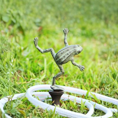 Aluminum dancing frog garden hose guide stake with hose looped around it in grass.