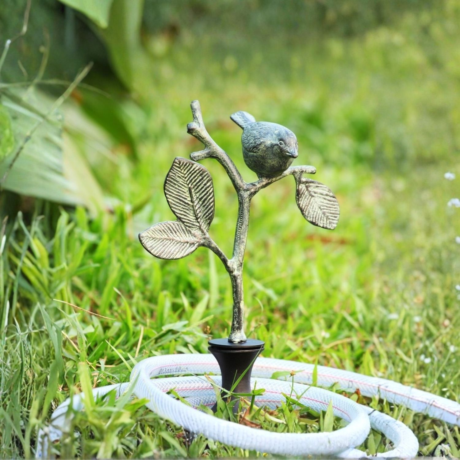Decorative bird on branch garden hose guide stake with hose resting against it in grass.