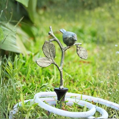 Decorative bird on branch garden hose guide stake with hose resting against it in grass.