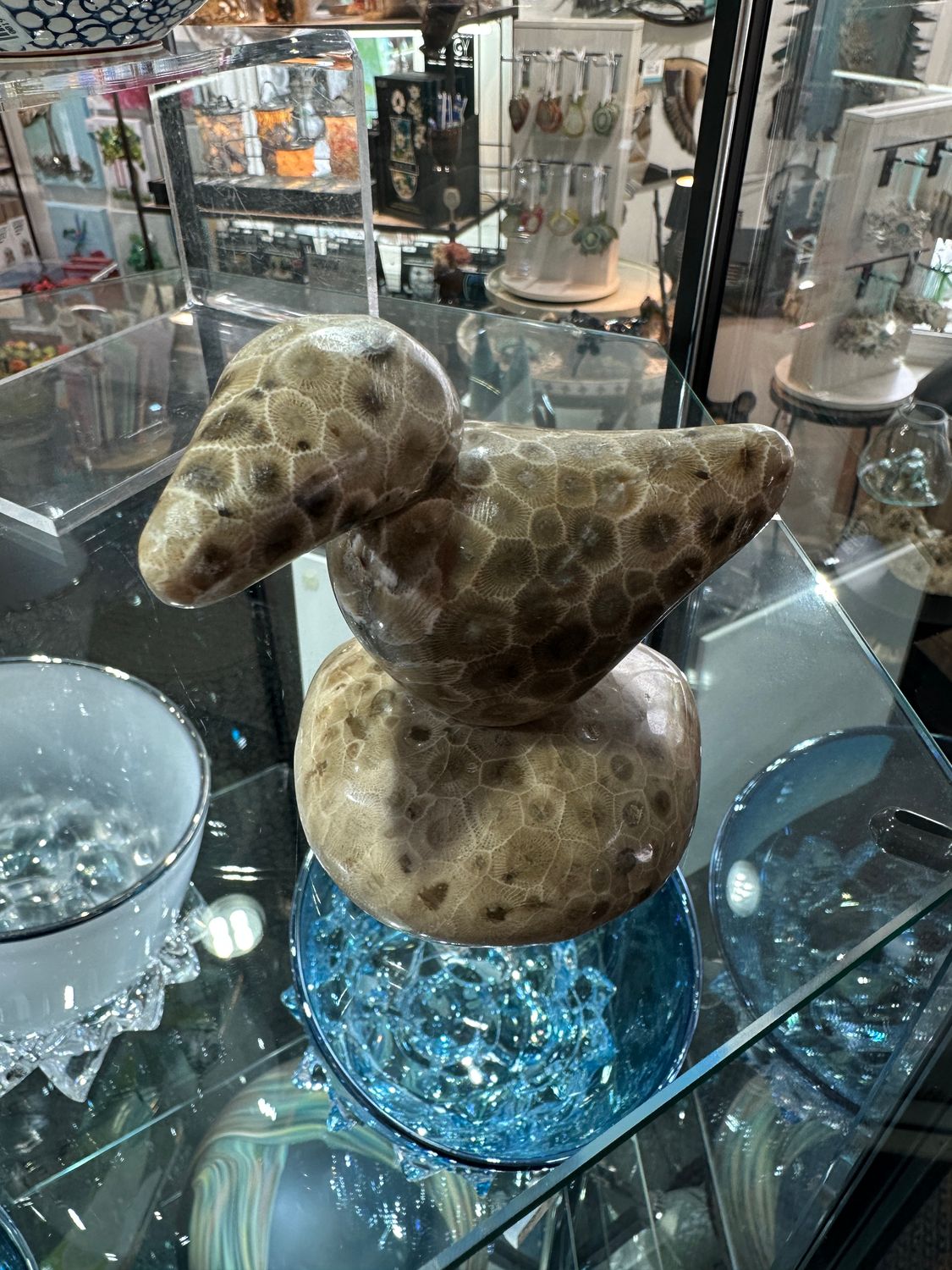 A handcrafted bird sculpture composed of three polished Michigan Petoskey stones displayed on a glass shelf.