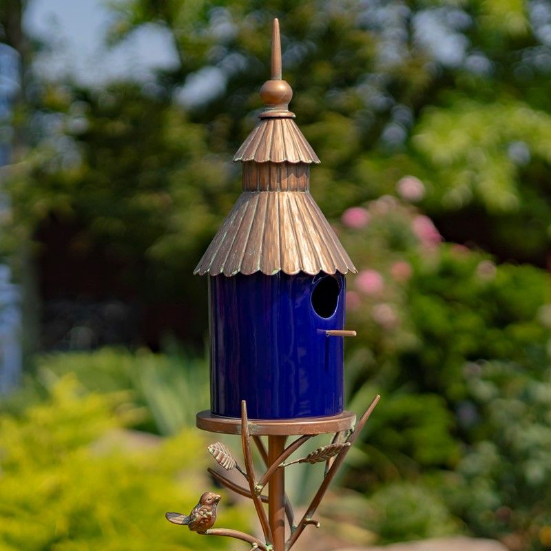 Cobalt blue porcelain birdhouse with an antique copper ornate roof mounted on a tall iron garden stake.