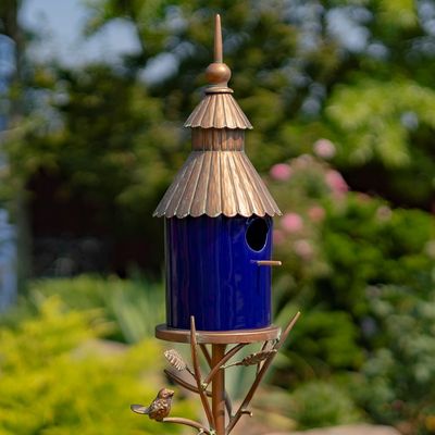 Cobalt blue porcelain birdhouse with an antique copper ornate roof mounted on a tall iron garden stake.