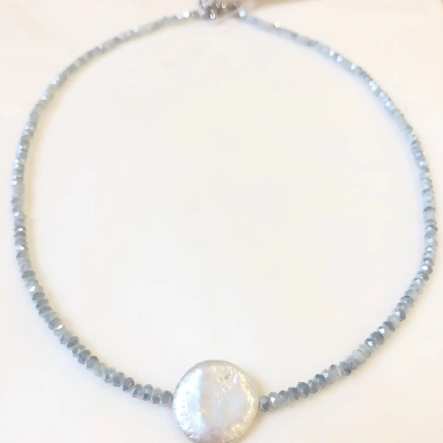 A delicate handmade necklace featuring icy frost blue crystal beads and a luminous, flat coin pearl pendant