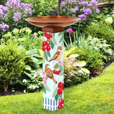 Vibrant bird bath art pole standing in a garden, featuring colorful artwork and a metallic copper topper.