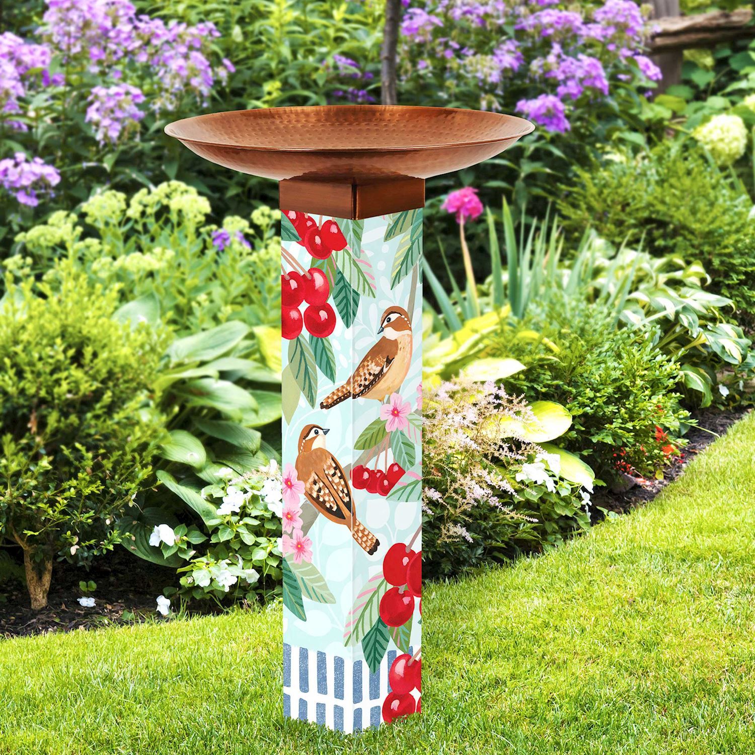 Vibrant bird bath art pole standing in a garden, featuring colorful artwork and a metallic copper topper.