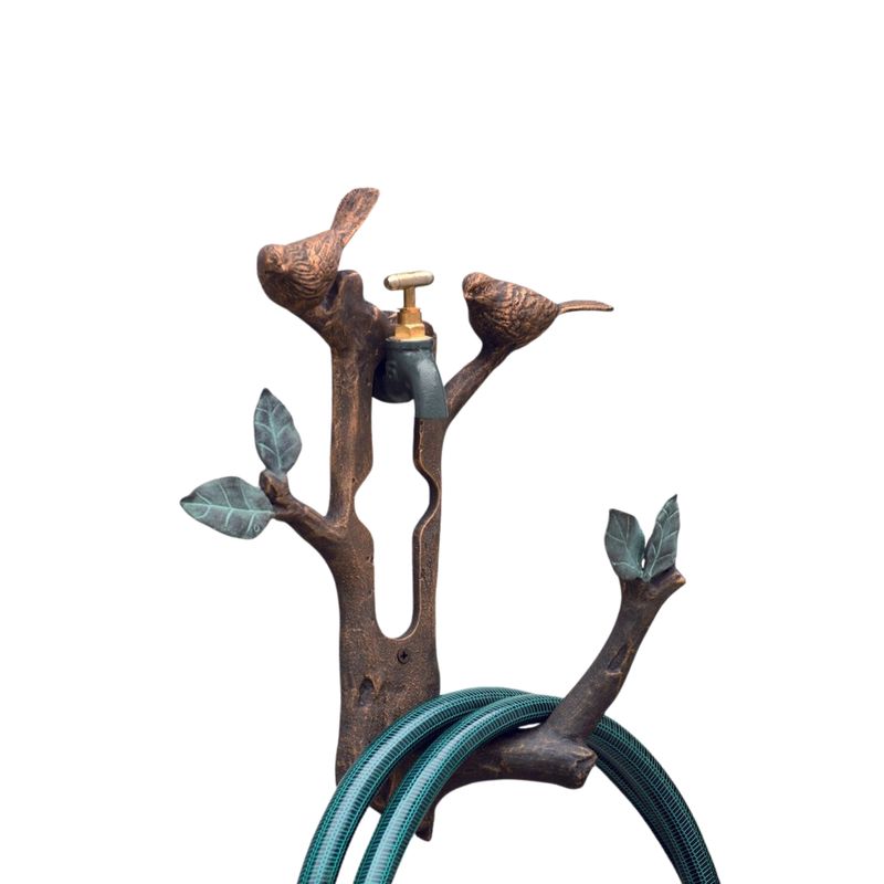 Decorative aluminum bird and branch wall-mounted hose holder with garden hose looped around base.
