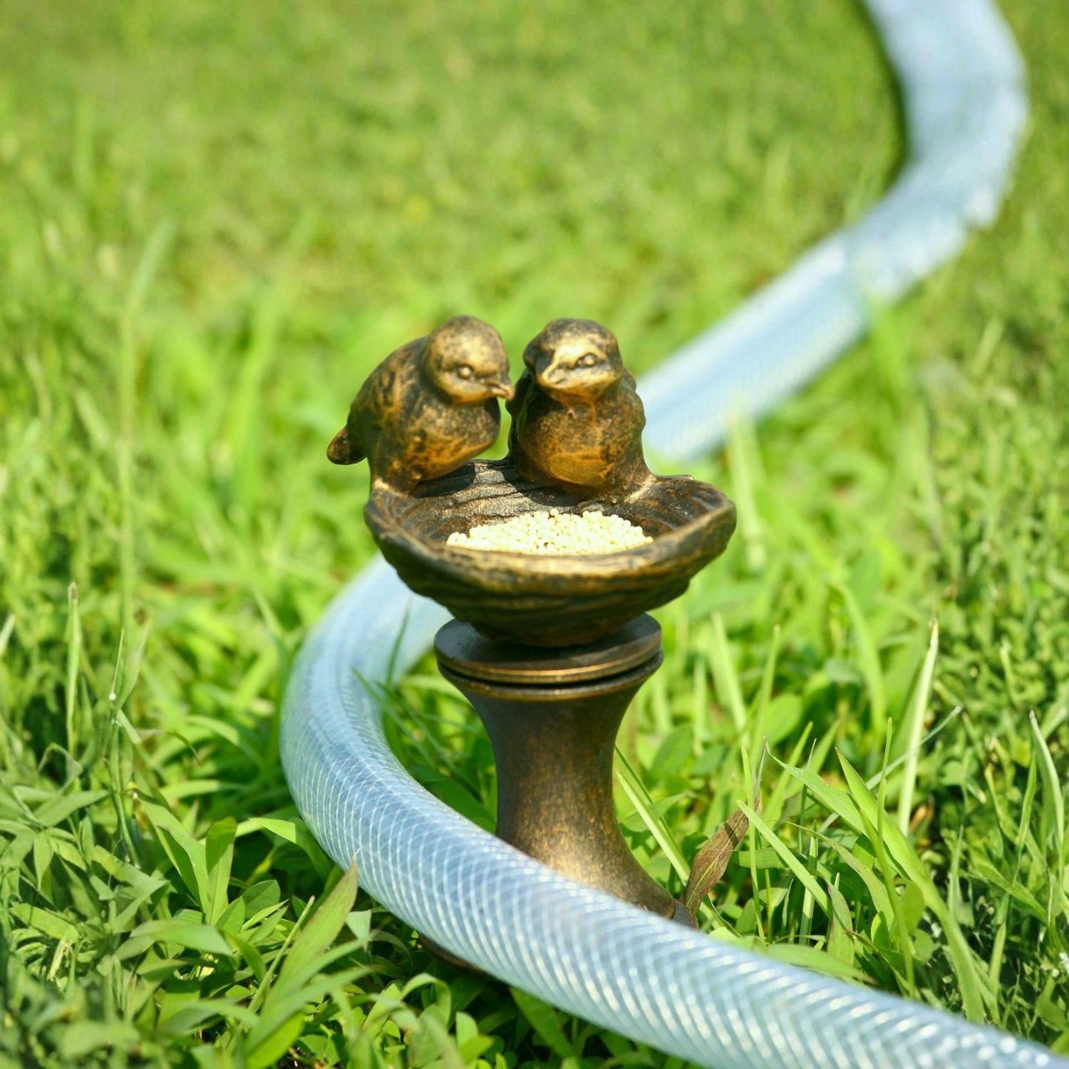 Aluminum lovebirds garden hose guide stake with hose resting against it in grass.
