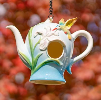 Blue and white porcelain teapot birdhouse with pink lilies and a green hummingbird figurine near the handle