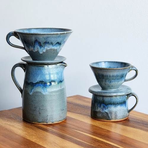 A handcrafted Lakeshore Grey glazed ceramic coffee pour-over set sitting on a matching ceramic pitcher.