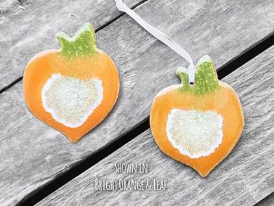 A bright orange peach-shaped ceramic hanging ornament featuring a vibrant green leaf accent and a loop attached
