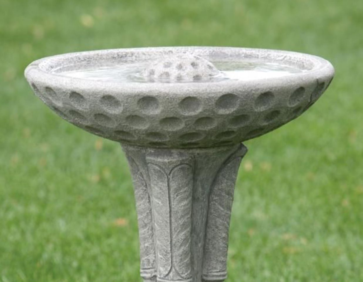 Cast stone bird bath with a white finish, featuring a shallow round basin on a pedestal with vertical "golf club" grooves.