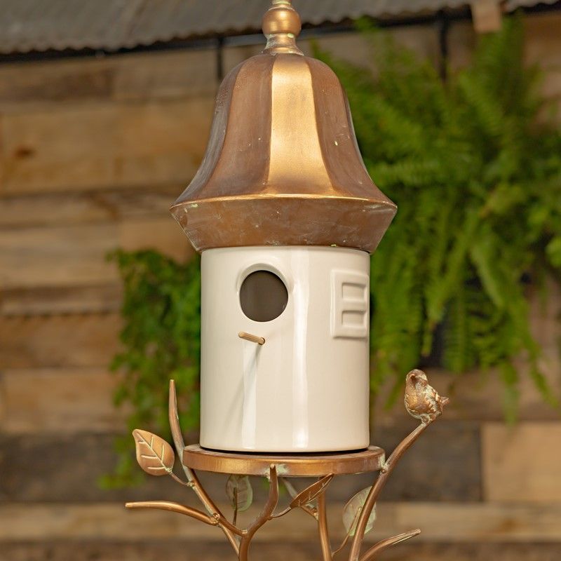 White porcelain hanging birdhouse with antique copper metal roof, decorative branches, leaves and small bird accent.
