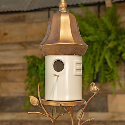 White porcelain hanging birdhouse with antique copper metal roof, decorative branches, leaves and small bird accent.