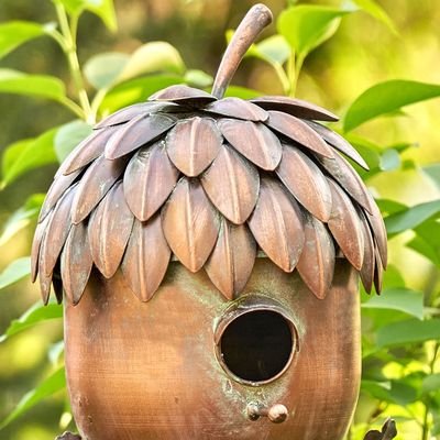 Acorn birdhouse stake styled in a garden bed with flowers and greenery.