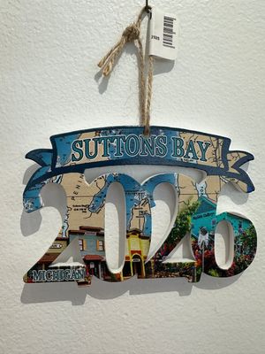 A laser-cut wooden ornament featuring a layered map design of Suttons Bay with "SUTTONS BAY" engraved across the top banner