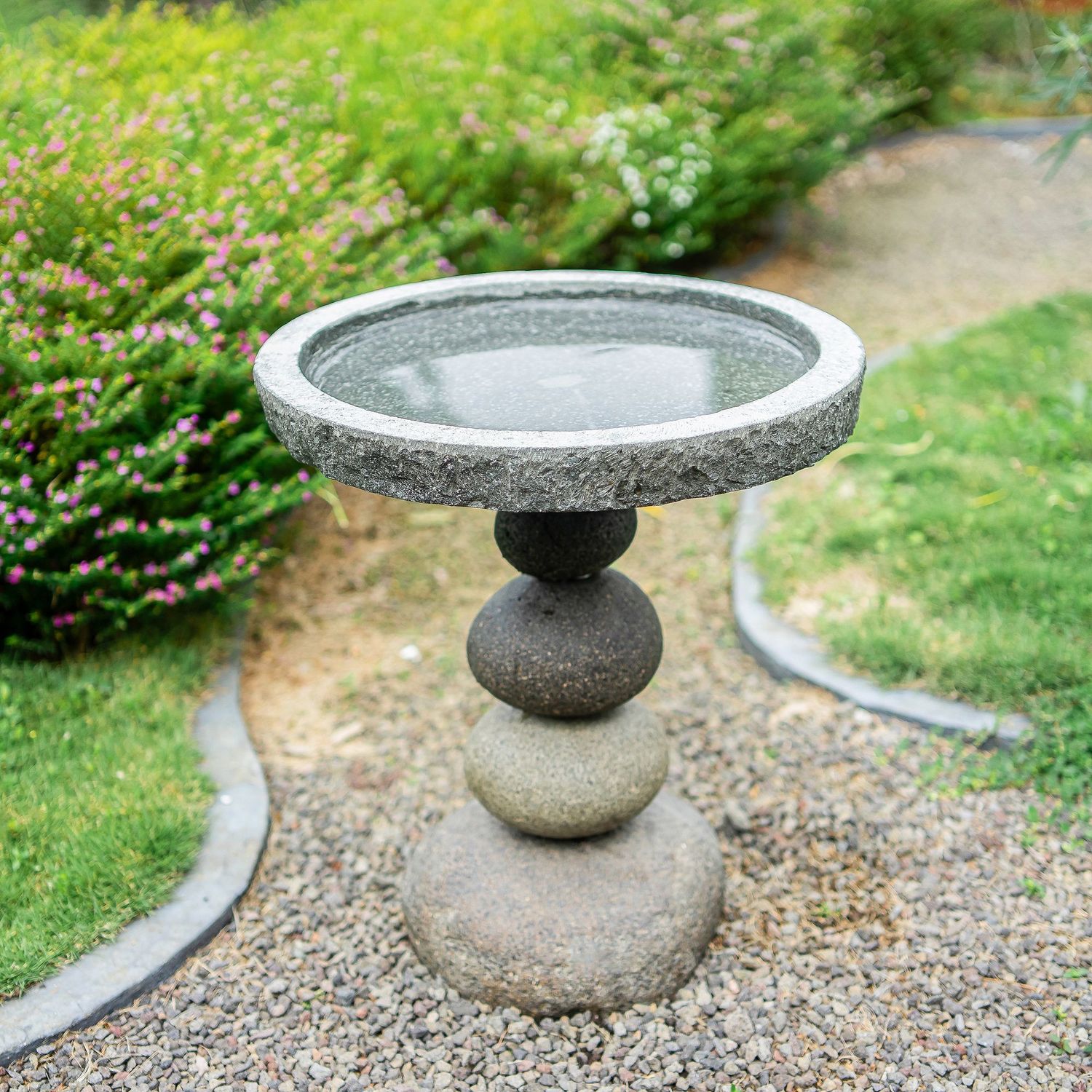 Rock cairn bird bath with a stacked stone pedestal base and a shallow, circular stone basin.