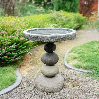 Side view of the rock cairn bird bath showing the natural grey stone textures in a garden setting.