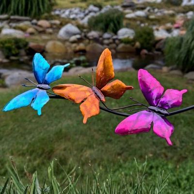 Close-up of three bright, saturated metal butterflies on a gentle kinetic balancing garden stake.