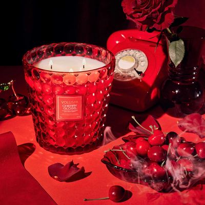 A lit Cherry Gloss Hearth candle illuminating a dark setting, showcasing the red glass's glow.