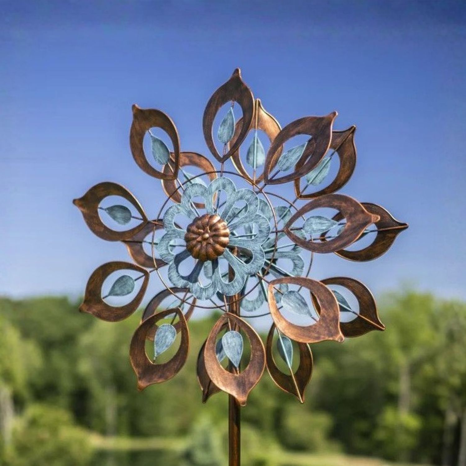 Bronze and soft blue dual motion wind spinner with leaf-shaped blades mounted on tall garden stake.
