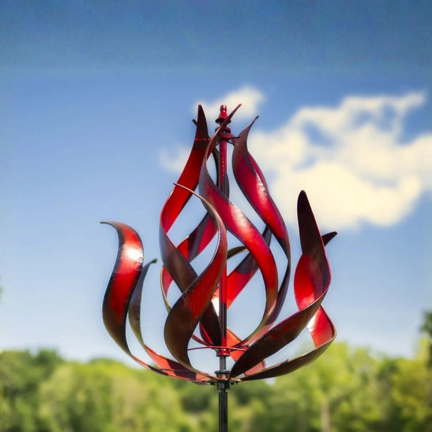 Red flame-style metal wind spinner with curved sculptural blades mounted on tall garden stake.
