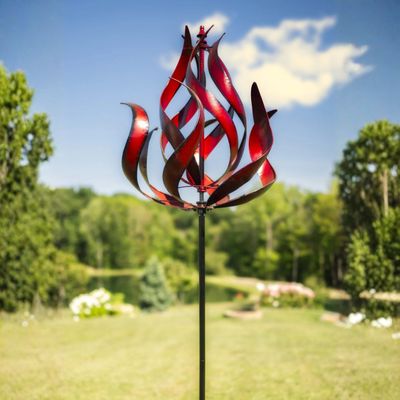 Tall red flame wind spinner displayed in grassy outdoor landscape setting.
