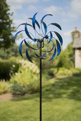 Blue Sedona metal wind spinner with layered curved blades mounted on tall garden stake outdoors.