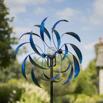 Blue Sedona metal wind spinner with layered curved blades mounted on tall garden stake outdoors.