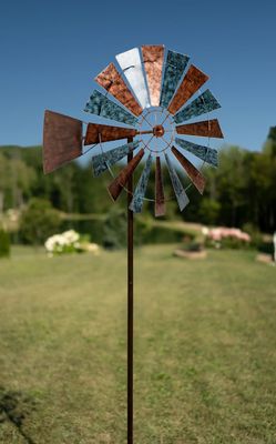 Prairie-style metal wind spinner with layered windmill blades and mixed finish mounted on tall garden stake in lawn.