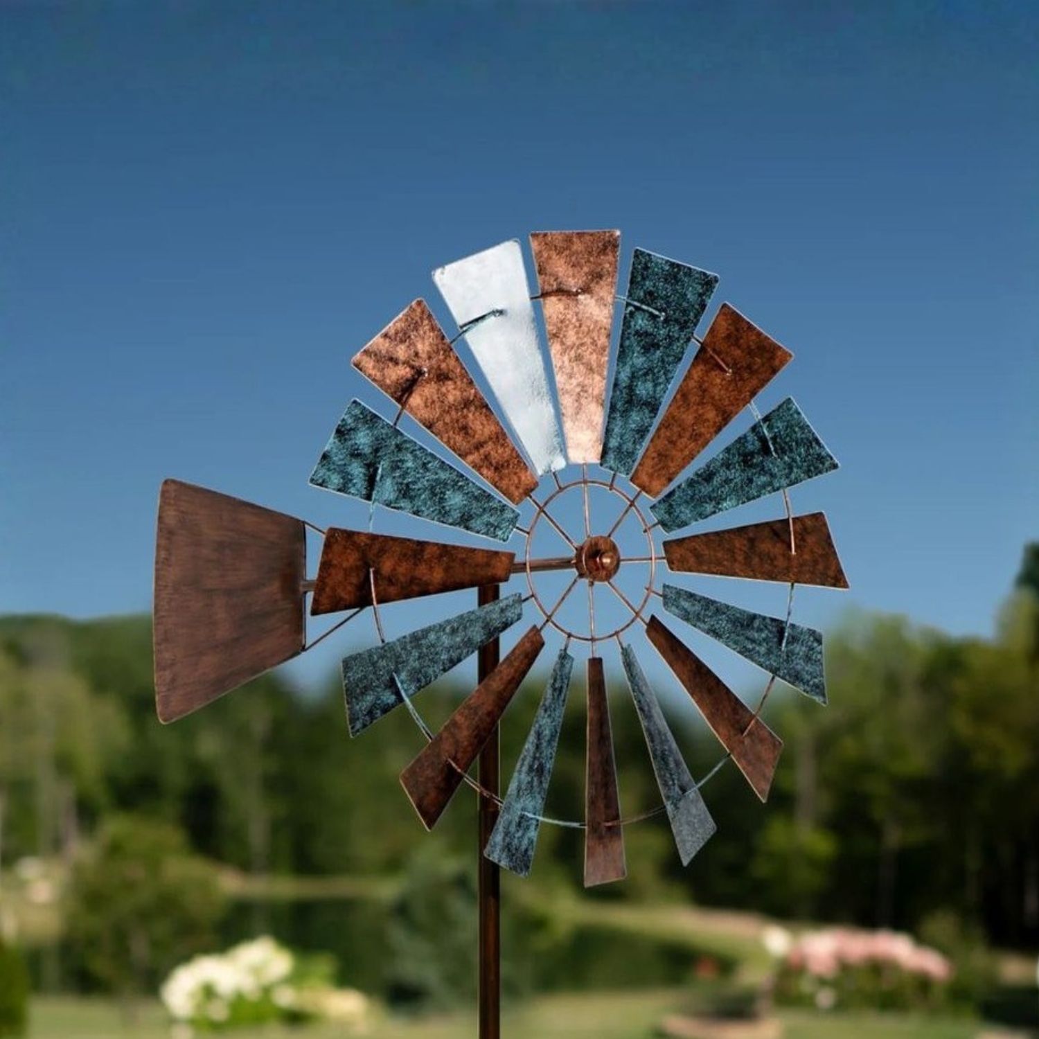 Prairie-style metal wind spinner with layered windmill blades and mixed finish mounted on tall garden stake in lawn.