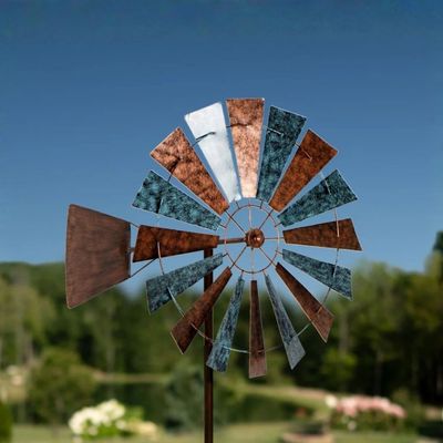 Prairie-style metal wind spinner with layered windmill blades and mixed finish mounted on tall garden stake in lawn.