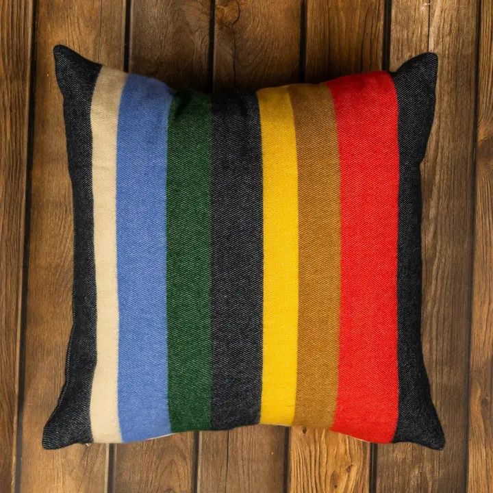 Multi colored striped cotton throw pillow displayed against a wood background.
