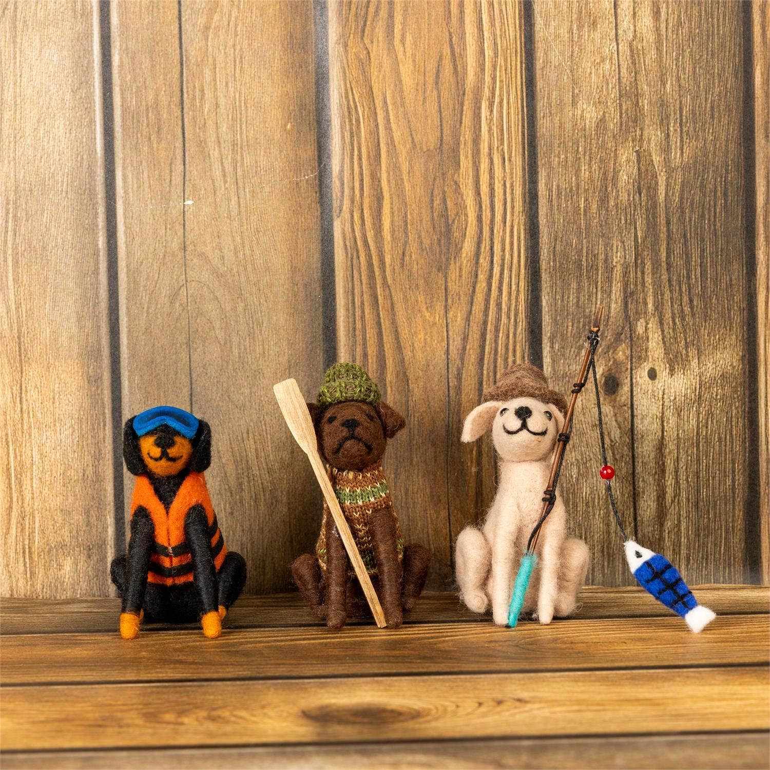 Felted wool fishing dog ornaments in three styles displayed on a wooden surface.