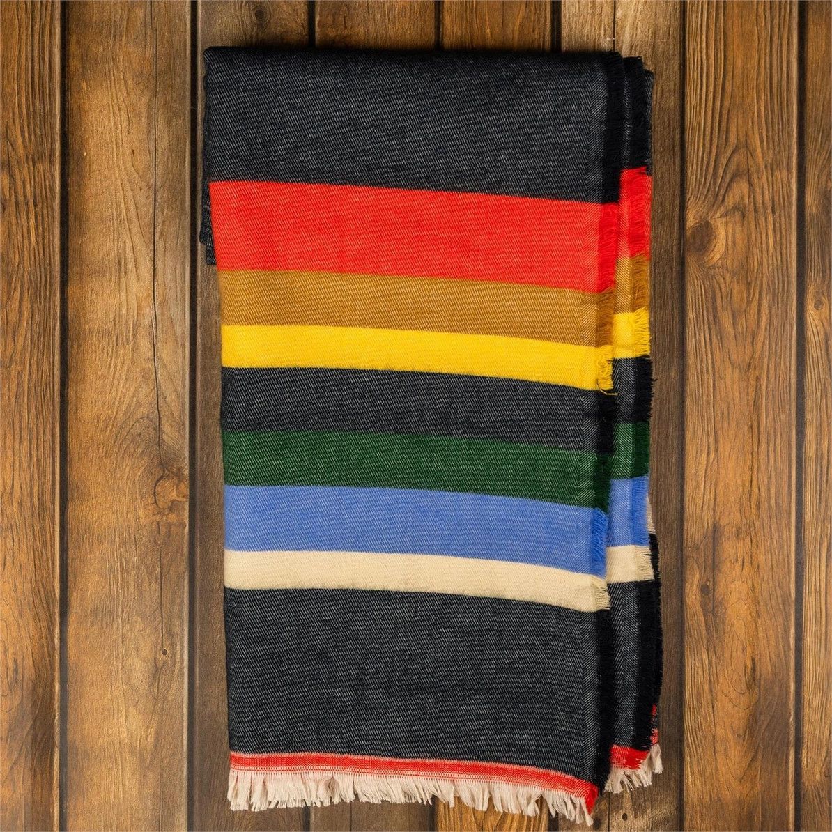 Woven multicolor striped throw blanket with fringe folded on a wooden surface.