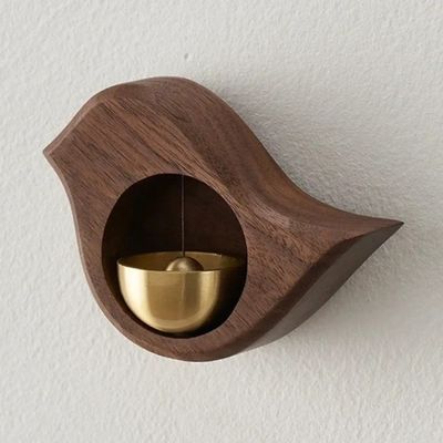 Wooden bird-shaped magnetic doorbell with brass bell in Walnut finish mounted on a light wall.