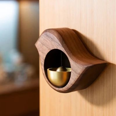 Wooden bird-shaped magnetic doorbell with brass bell in Walnut finish mounted on a an open door.