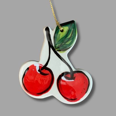 Hand painted ceramic cherry ornament with two red cherries and green leaf hanging from a gold cord.