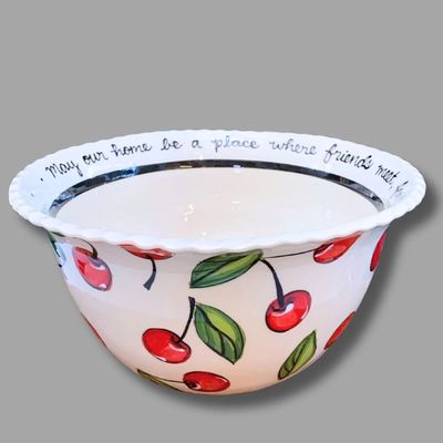 Side view of ceramic bowl with red cherries and green leaves on cream background.