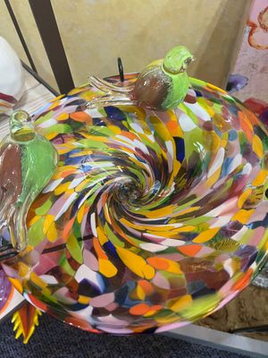 Close-up top view of a colorful multi-opaque glass birdbath bowl showing an intricate swirling pattern of yellow, red, blue