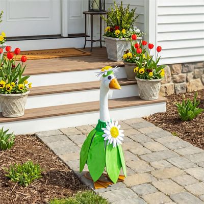 Giddy the Porch Goose wearing a green daisy outfit and flower headpiece on a stone walkway beside front steps.