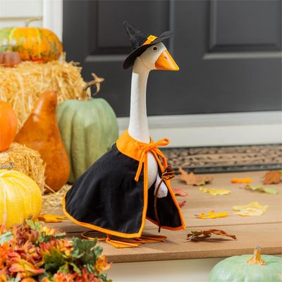 Giddy the Porch Goose wearing a black witch cape and pointed hat beside pumpkins, hay bales, and fall leaves.