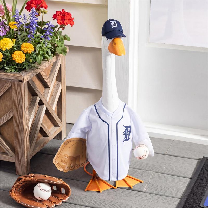 Giddy in a Detroit Tigers uniform beside a flower planter, with a baseball and glove resting on the porch nearby.