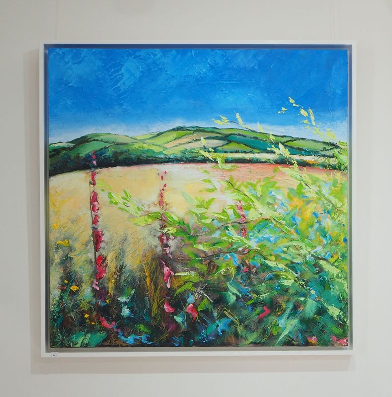 Square painting of a field with rolling hills in the background. The sky is a bright blue with a light highlight framing the hills. The field is almost gold in colour and feels warm. We are looking through foliage in the foreground which feels cool. The bust texture of the foliage suggests Foxgloves and Buddleia.