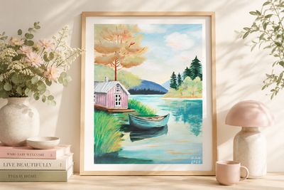 Handgeschilderde kunstprint van een roze huisje aan het water, gepresenteerd in een licht houten frame in een pastelkleurig i