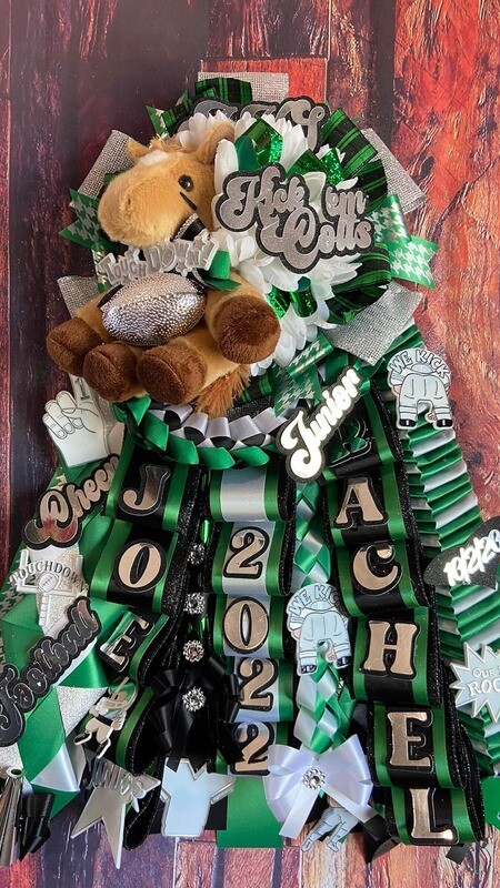A decorative Homecoming Garter featuring ribbons, a plush horse, and text reading &quot;Kick &#39;Em Colts,&quot; &quot;Forever Friends,&quot; &quot;Rachel,&quot; and &quot;2022&quot; in vibrant green, silver, and black tones.
