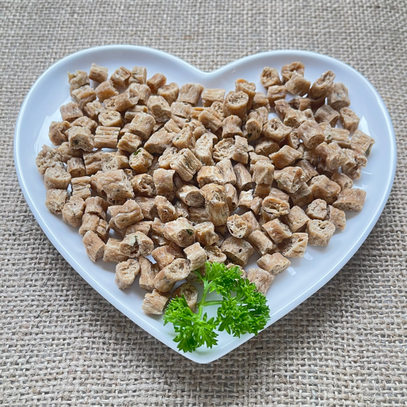Small bite sized cat treats displayed with a sprig of parsley on a white heart shaped plate.