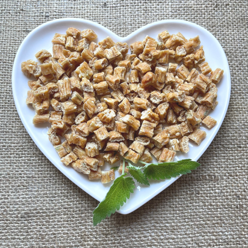 Small bite sized cat treats displayed with a sprig of catnip on a white heart shaped plate.