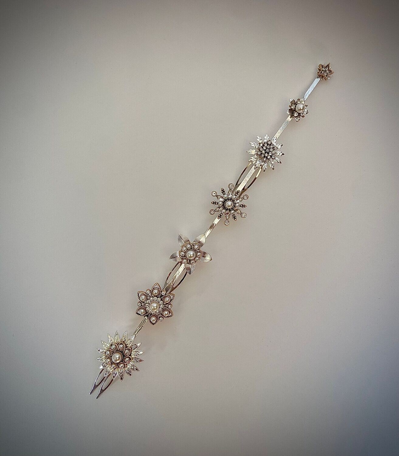 Cubreraíz en base plata compuesto por 7 flores con detalles centrales en tonos plata y dorado envejecido con perlas y cristales transparentes. Tiene una longitud de unos 25 cm aproximadamente.

Puede acompañarse de horquillas a conjunto para completar el look y dar un toque chic al peinado. Es una pieza en tendencia actualmente por ofrecer un punto de luz cercano al rostro.