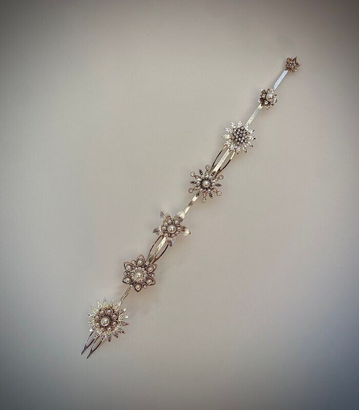Cubreraíz en base plata compuesto por 7 flores con detalles centrales en tonos plata y dorado envejecido con perlas y cristales transparentes. Tiene una longitud de unos 25 cm aproximadamente.

Puede acompañarse de horquillas a conjunto para completar el look y dar un toque chic al peinado. Es una pieza en tendencia actualmente por ofrecer un punto de luz cercano al rostro.